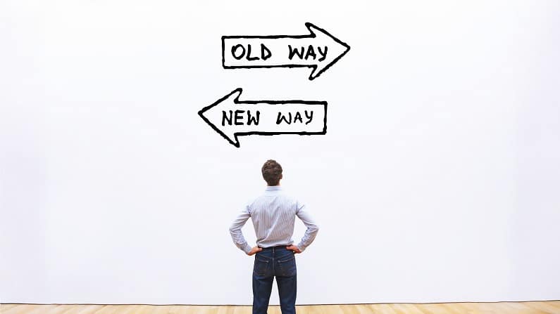 Interim management is symbolised by a man with his back to a white wall. On the wall, two arrows point in opposite directions. One indicates old way. The other points to the new way.