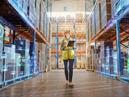L'illustration de l'article sur le lean logistic met en scène une femme portant un gilet jaune et un casque de sécurité qui marche dans une allée d'entrepôt, tablette en main pour le contrôle numérique des stocks.